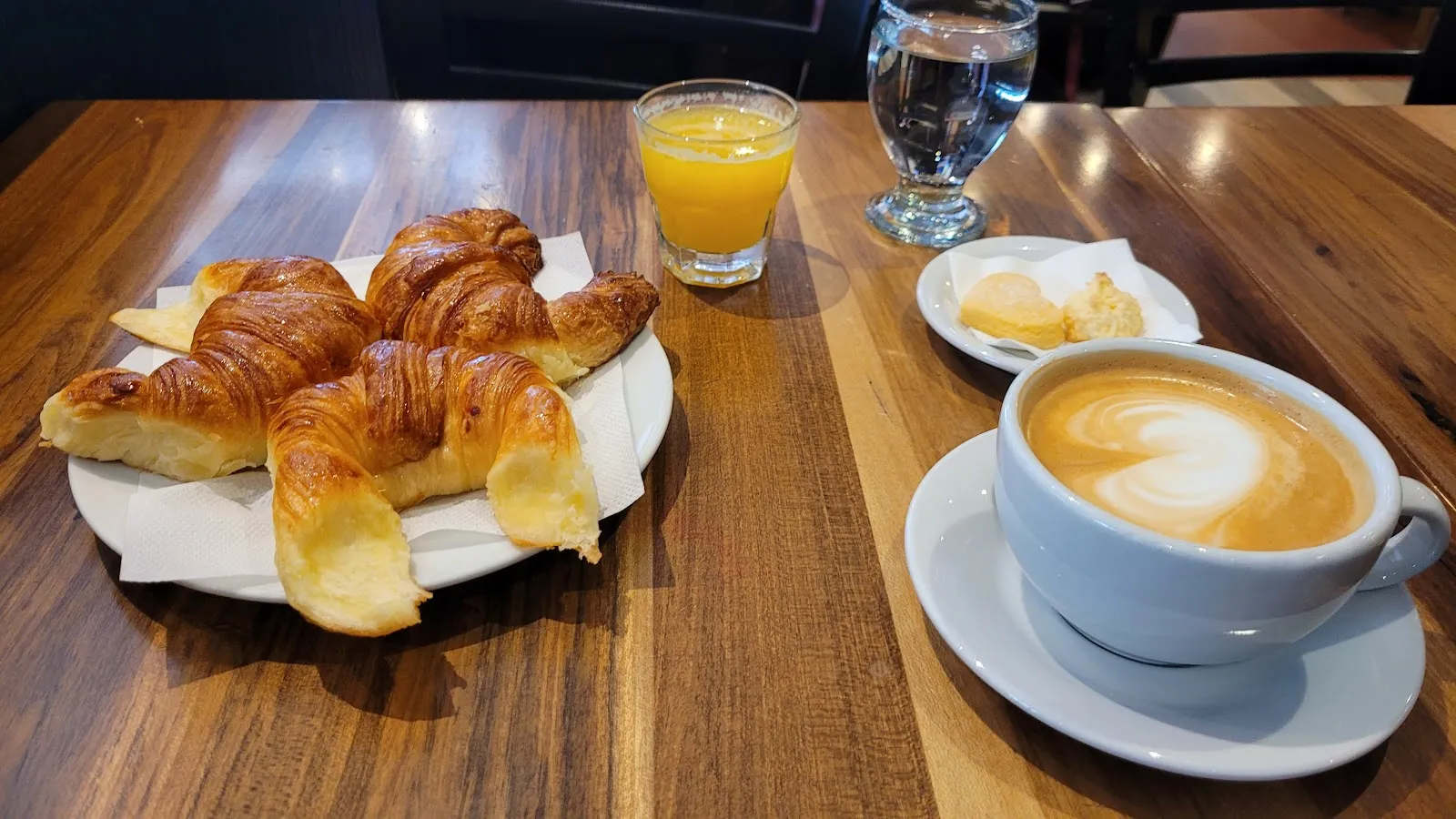 Medialunas, jugo de naranja y café con leche sobre mesa de madera
